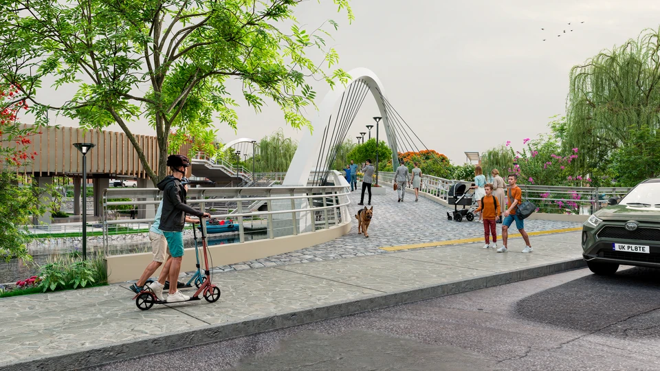 Entrada a un puente peatonal de arco blanco; familias caminan, un niño va en scooter y un perro cruza, junto a la pista con un auto.