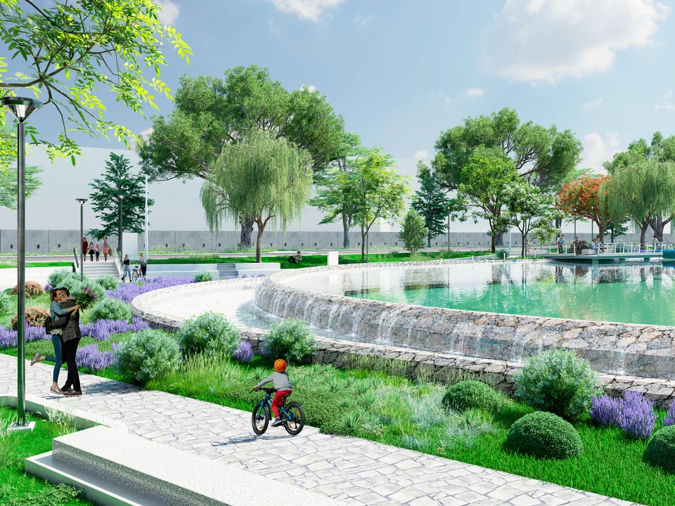 Estanque circular con bordes escalonados por donde cae el agua, rodeado de césped, lavandas y árboles; un niño pasea en bicicleta.